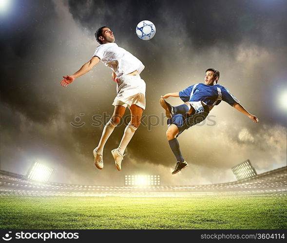 two football players in jump to strike the ball at the stadium