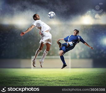 two football players in jump to strike the ball at the stadium