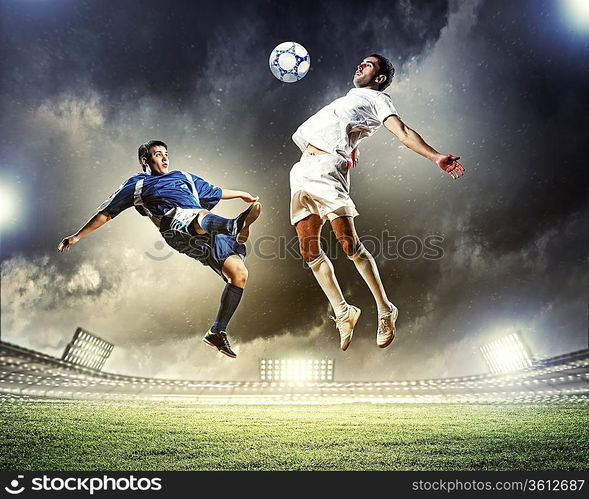 two football players in jump to strike the ball at the stadium