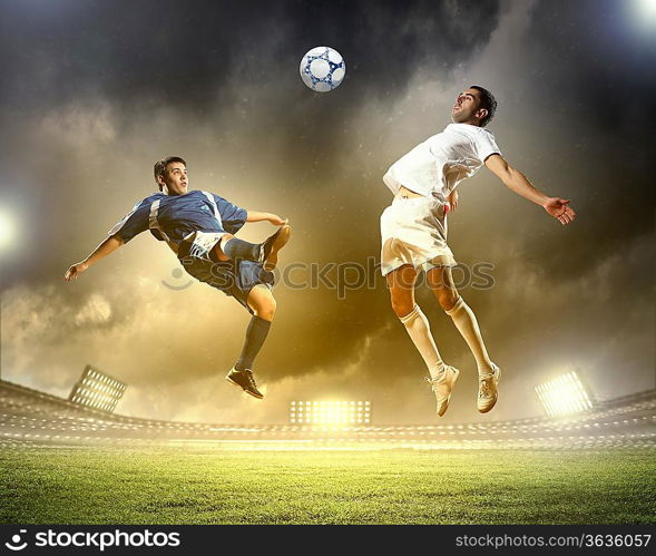 two football players in jump to strike the ball at the stadium