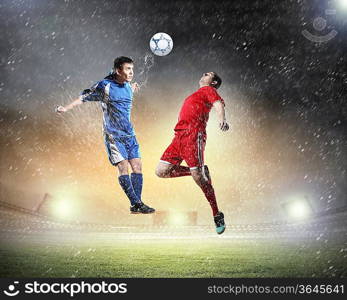 two football players in jump to strike the ball at the stadium