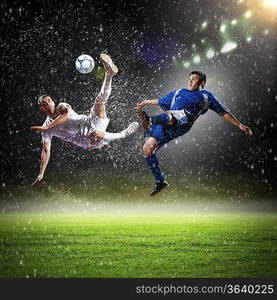 two football players in jump to strike the ball at the stadium under rain