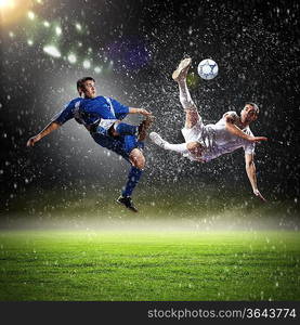 two football players in jump to strike the ball at the stadium under rain