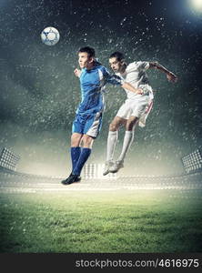 two football players striking the ball. two football players in jump to strike the ball at the stadium under rain