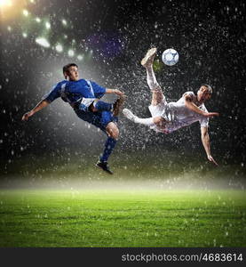 two football players striking the ball. two football players in jump to strike the ball at the stadium under rain