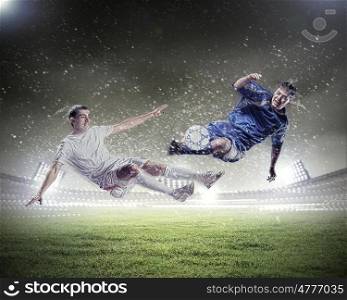 two football players striking the ball. two football players in jump to strike the ball at the stadium under rain