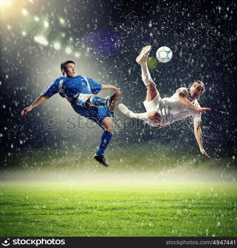 two football players striking the ball. two football players in jump to strike the ball at the stadium under rain