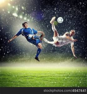 two football players striking the ball. two football players in jump to strike the ball at the stadium under rain