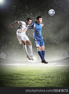 two football players striking the ball. two football players in jump to strike the ball at the stadium under rain