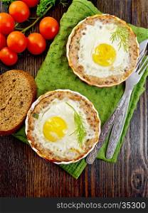 Two forms of tartlets with meat and eggs in the forms on a napkin, tomatoes, bread, parsley and dill on background of wood planks top