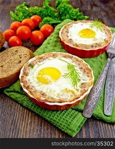 Two forms of tartlets with meat and eggs in the forms on a napkin, tomatoes, bread, parsley and dill on background of dark wood planks