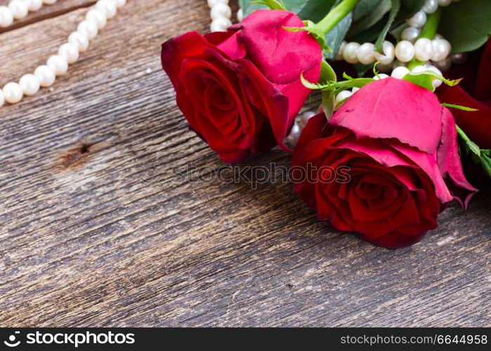 two fresh red rose flowers  with  pearls on wooden table close up. red roses on table 