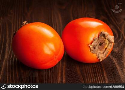 Two fresh ripe orange persimmon on a wooden background