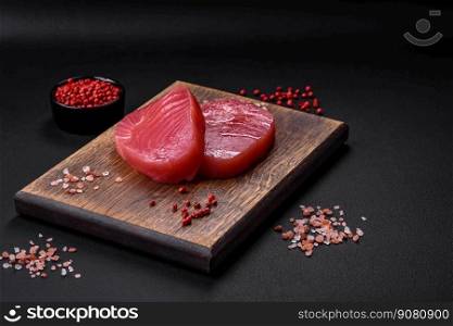 Two fresh slices of raw tuna fillet with spices and herbs on a dark concrete background