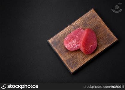 Two fresh slices of raw tuna fillet with spices and herbs on a dark concrete background