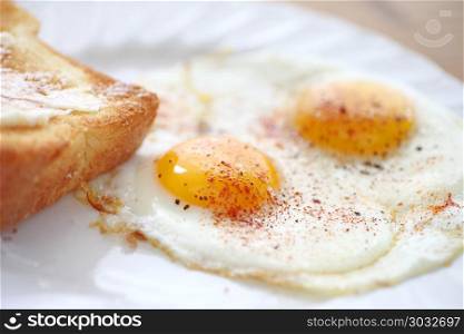 two fried eggs sunny side up, sprinkled with smoked paprika and black pepper, toast alongside. Fried eggs with smoked paprika and toast