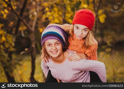 Two friendly sisters playing with autumn leaves and smiling. Sisters playing with leaves