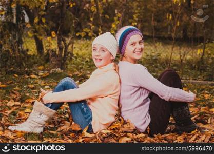 Two friendly sisters playing with autumn leaves and smiling. Sisters playing with leaves