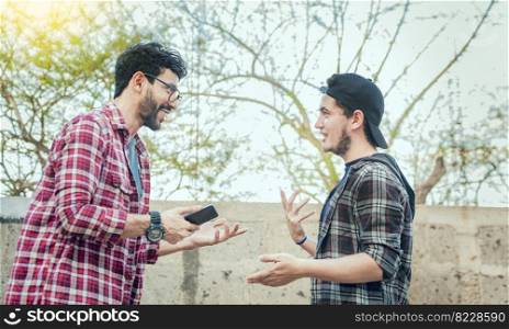 Two friends chatting while smiling and using cellphone. View of two teenagers talking face to face while using the cell phone, Side view of two young friends chatting outdoors