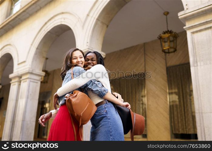 Two friends happy to see each other on the street hugging. Multiethnic women.. Two friends happy to see each other on the street hugging.