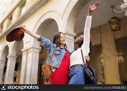 Two friends happy to see each other on the street hugging. Multiethnic women.. Two friends happy to see each other on the street hugging.