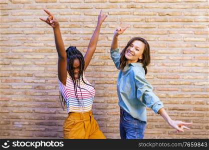 Two friends having fun together showing sign of the horns. Multiethnic women.. Two multiethnic women having fun together showing sign of the horns.