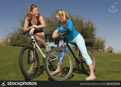 Two friends lean on their bikes talking