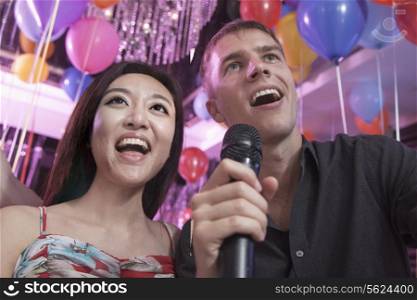 Two friends singing into a microphone together in a nightclub for karaoke