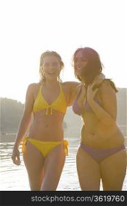 Two friends stand laughing in swimwear at dawn