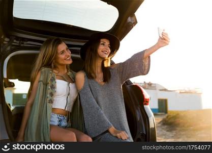 Two friends taking a selfie while sitting in the trunk of a car