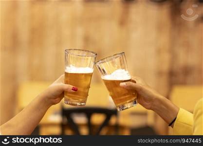 Two friends toasting with glasses of light beer at the pub. Beautiful background of the Oktoberfest