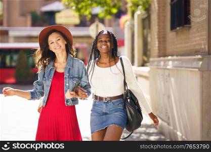 Two friends walking together on the street. Multiethnic women.. Two female walking together on the street. Multiethnic friends.