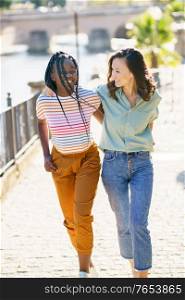 Two friends walking together on the street. Multiethnic women.. Two Multiethnic women walking together on the street.