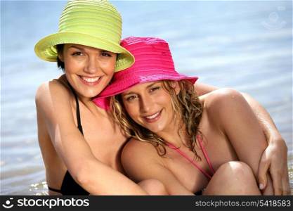 Two friends wearing hats and bikinis at the beach