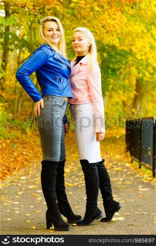 Two friends women wearing fashionable outfit. Female having navy bue pink leather jacket, jeans and high ankle black boots.. Females wearing fashionable autumn outfits