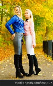 Two friends women wearing fashionable outfit. Female having navy bue pink leather jacket, jeans and high ankle black boots.. Females wearing fashionable autumn outfits