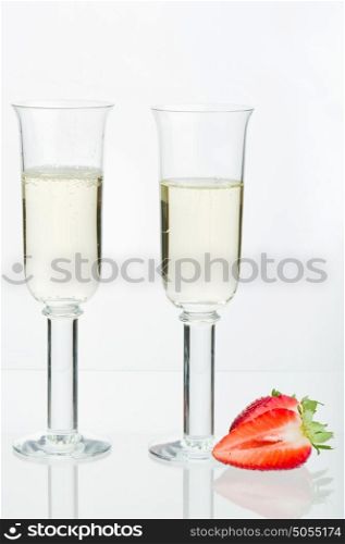 Two fulls sparkling glass, split strawberry, reflection and white background.