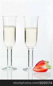 Two fulls sparkling glass, split strawberry, reflection and white background.