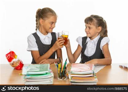 Two funny schoolgirls at a table drink juice, and banged glasses