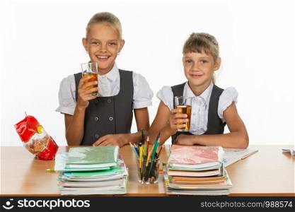 Two funny schoolgirls at a table drink juice, and look in the frame