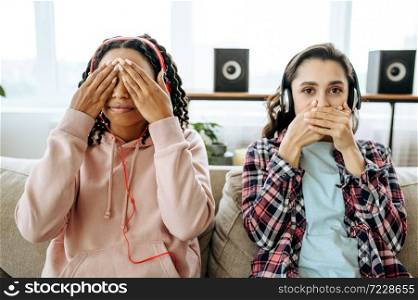 Two funny women jokes and listening to music at home. Pretty girlfriends in earphones relax in the room, sound lovers resting on couch, female friends leisures together. Funny women jokes and listening to music at home