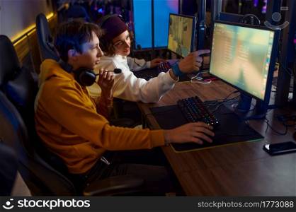Two gamers in headsets play in game club. Virtual entertainment, e-sport tournament, cybersport lifestyle. Male person leisures in internet cafe. Two gamers in headsets play in game club
