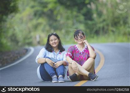 two generation of asian woman sitting on asphalt road in khao yai national park thailand