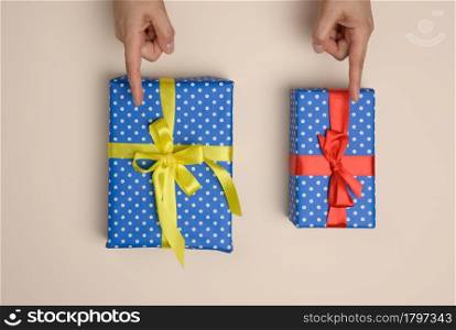 two gift boxes wrapped in a silk ribbon on a beige background, female fingers indicate choice