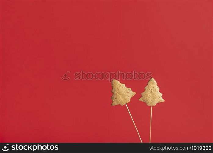 Two gingerbread cookies in Christmas tree shape, on skewers, on a red background. Traditional Xmas sweets. American Christmas desserts.