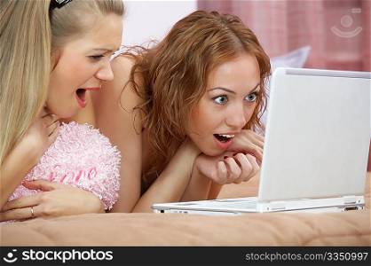 Two girl-friends in a shock look in the laptop screen