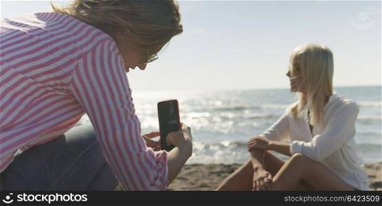Two Girl Friends Taking Photo with Smartphone On Empty Beach during autumn day