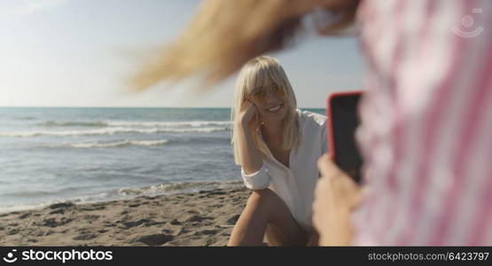 Two Girl Friends Taking Photo with Smartphone On Empty Beach during autumn day