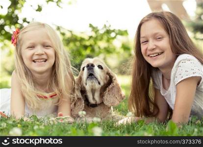 two girl sisters with dog lying on a grass