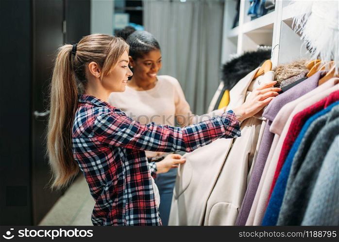 Two girlfriends choosing clothes in shop, shopping. Shopaholics in clothing store, consumerism lifestyle, fashion. Two girlfriends choosing clothes in shop, shopping